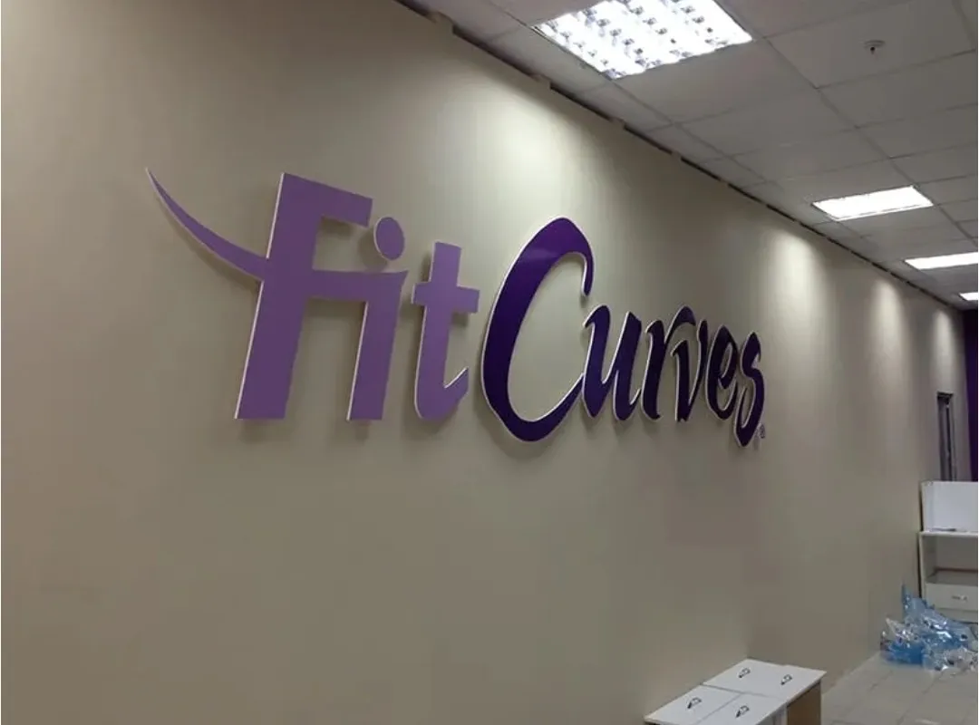 Фиолетовый логотип FitCurves на стене
